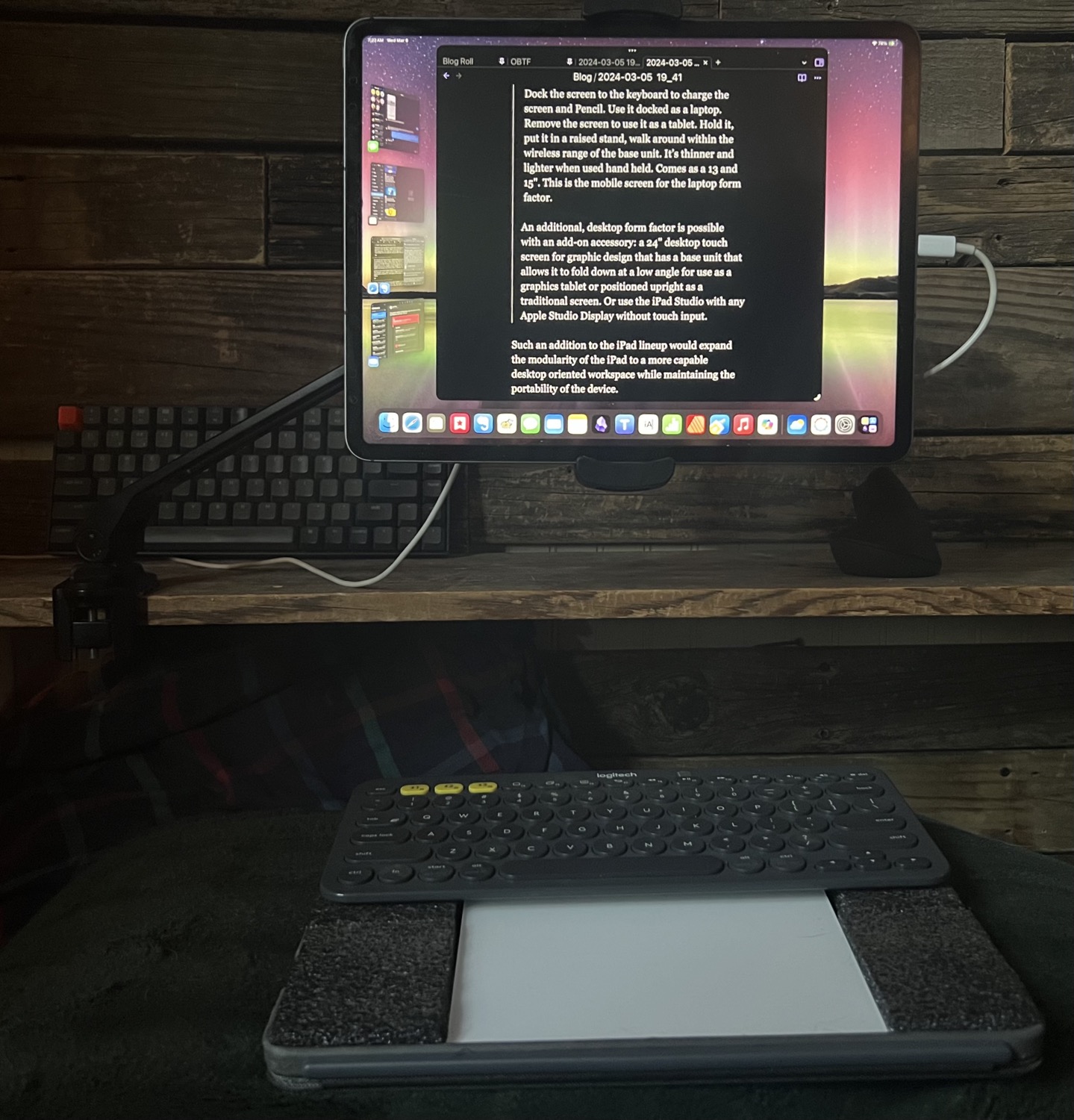 An iPad Pro is held in a stand clamped to a shelf. Below it is a keyboard and trackpad that are arranged on a small self-contained case