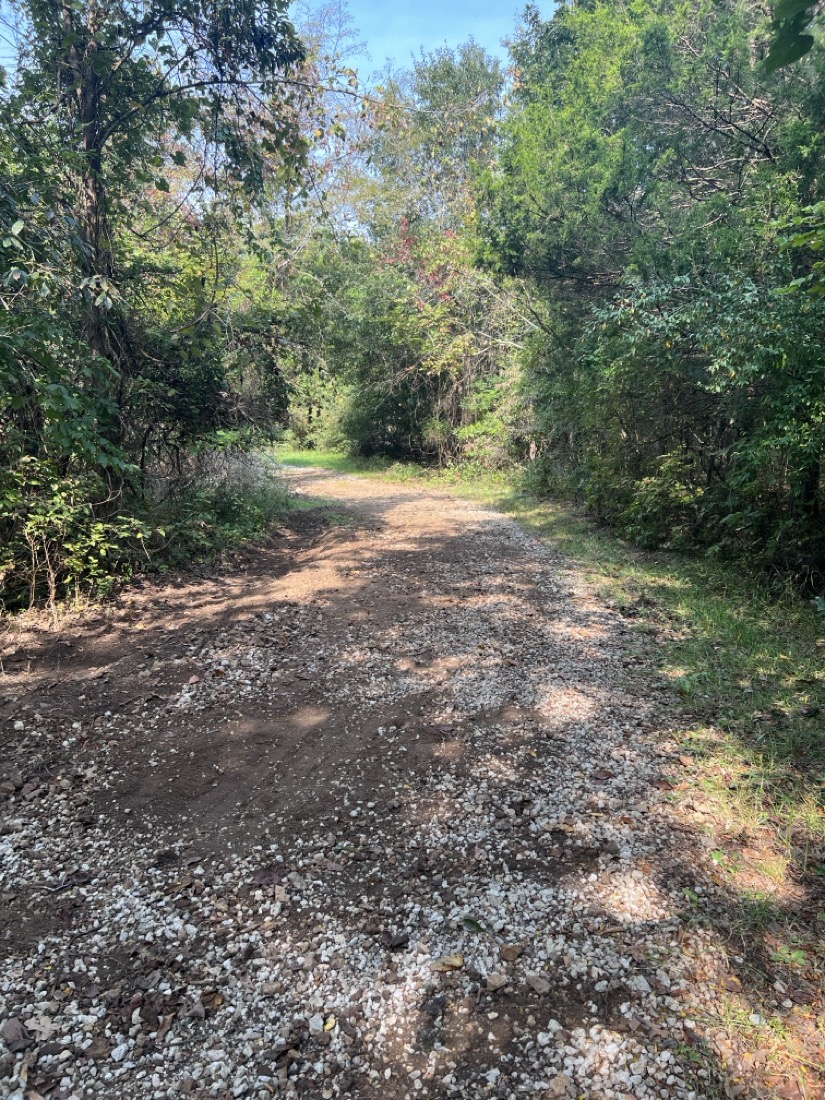 A gravel road with a ditch being dug on the left side