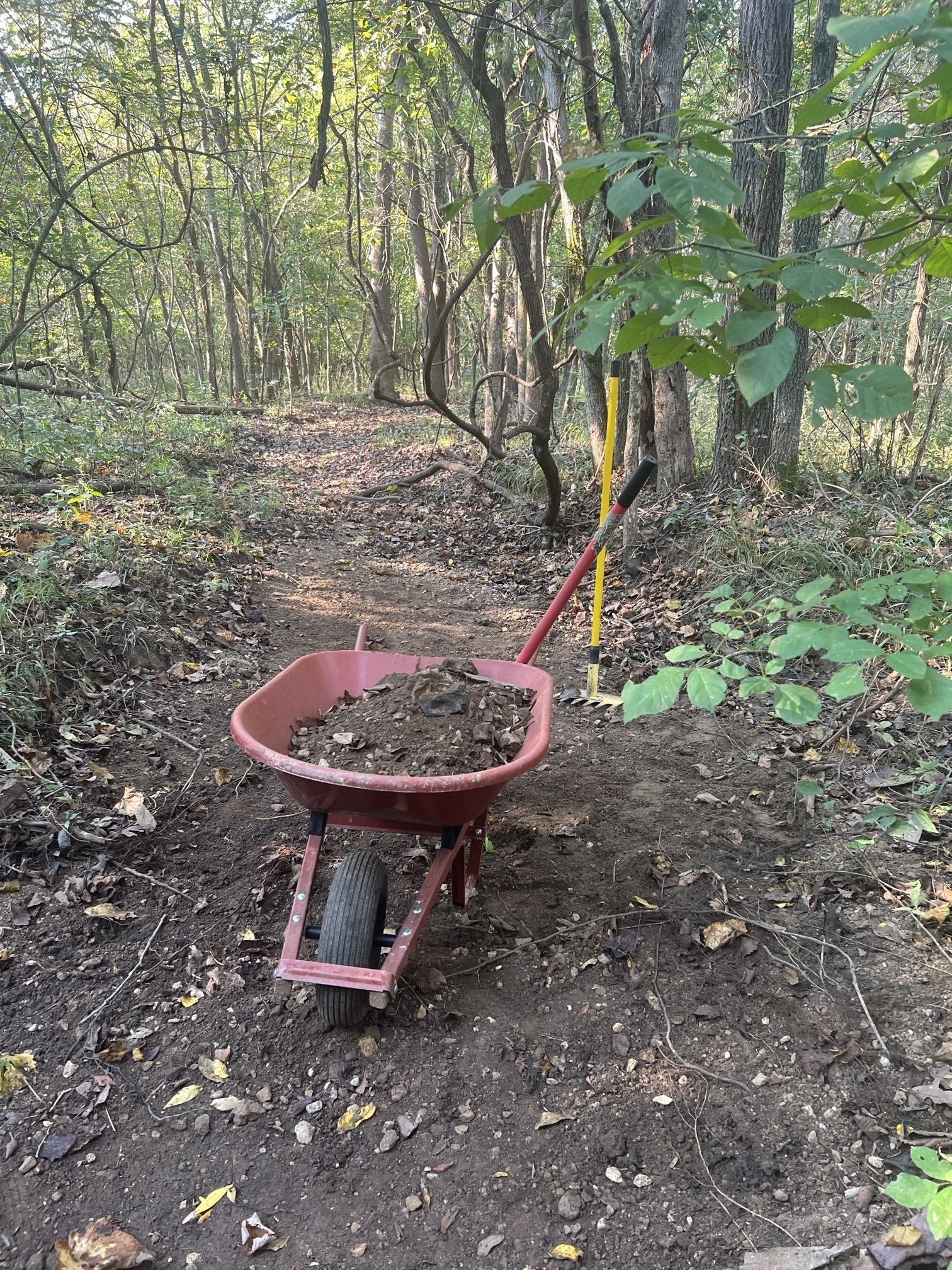 A wheelbarrow of dark colored sand, gravel and rocks sits in a dry creekbed