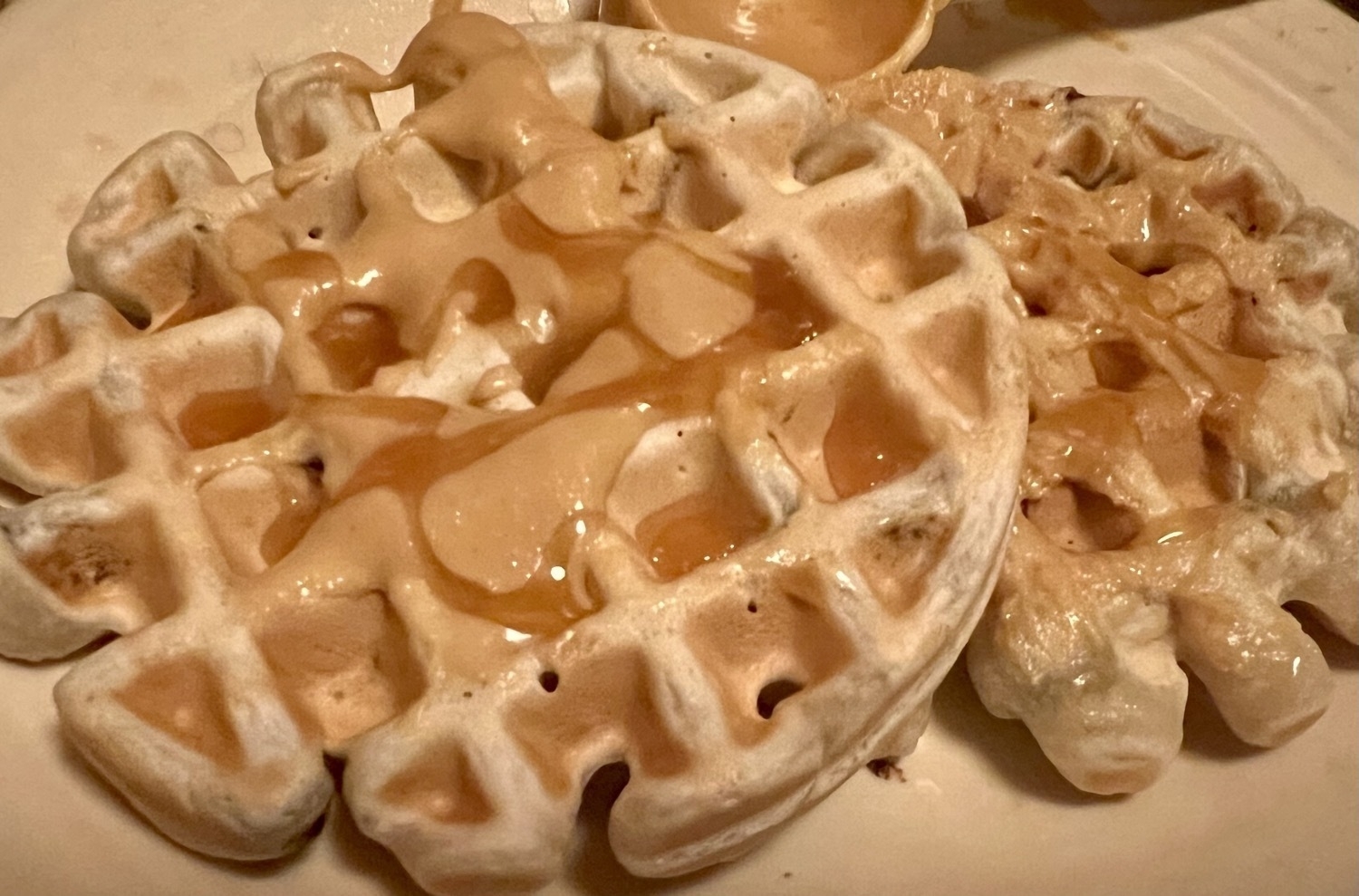 two waffles, on a plate with peanut butter and caramel on top