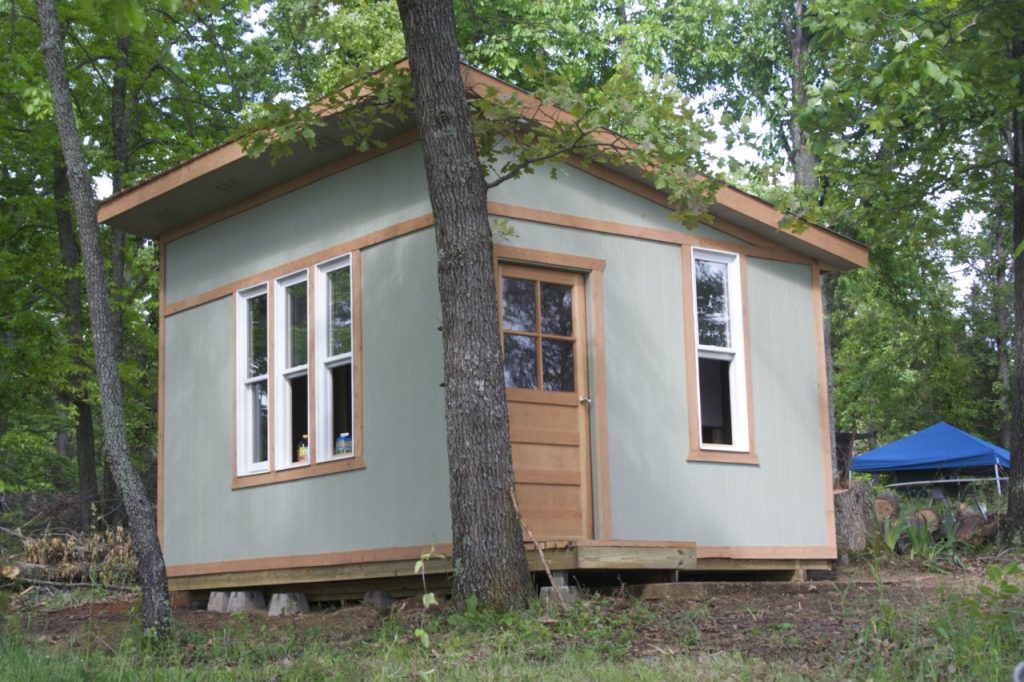 The cabin shell completed with windows and a door. It is painted a pale green te color of lichen with light brown trim