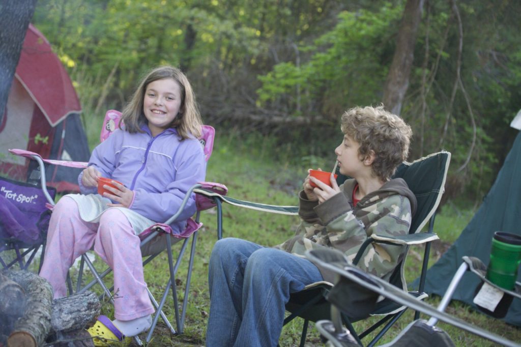 Camping during construction. My niece and nephew, 2 kids sitting in camping chairs talking together. The girl is looking at the camera