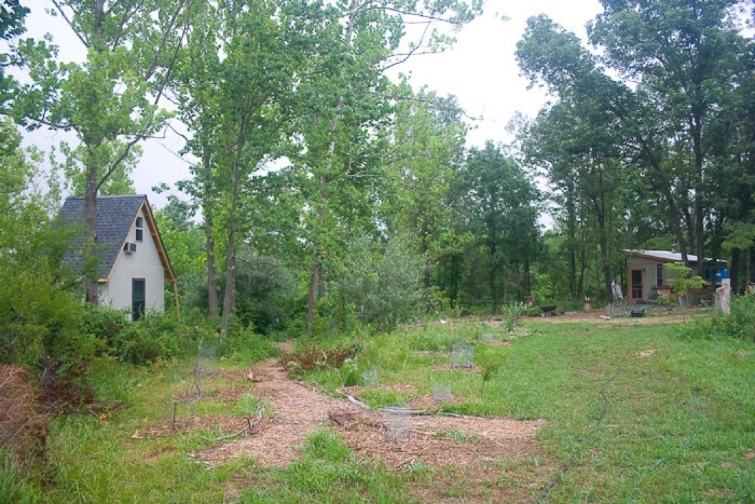 Various mulched paths with grass on the right side, two tiny house buildings in the background”