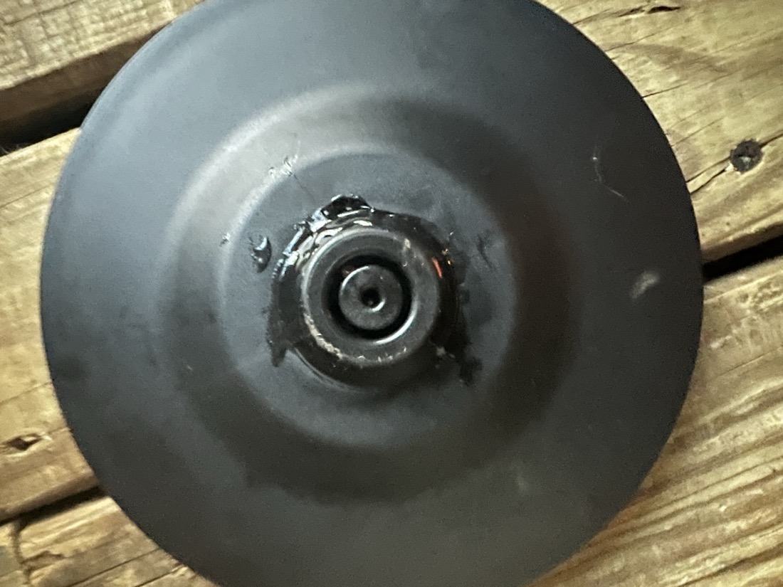 A black plastic disk with a molded circular center is raised up from the flat disk. That raised section has what appears to be a small stem or knob with a groove and a smaller center circle within that.