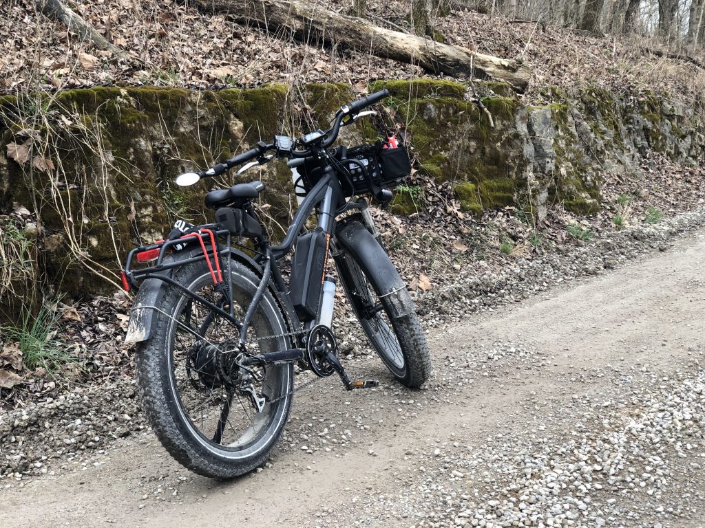 A black fat tire bike on a gravel road near a moss covered rock wall