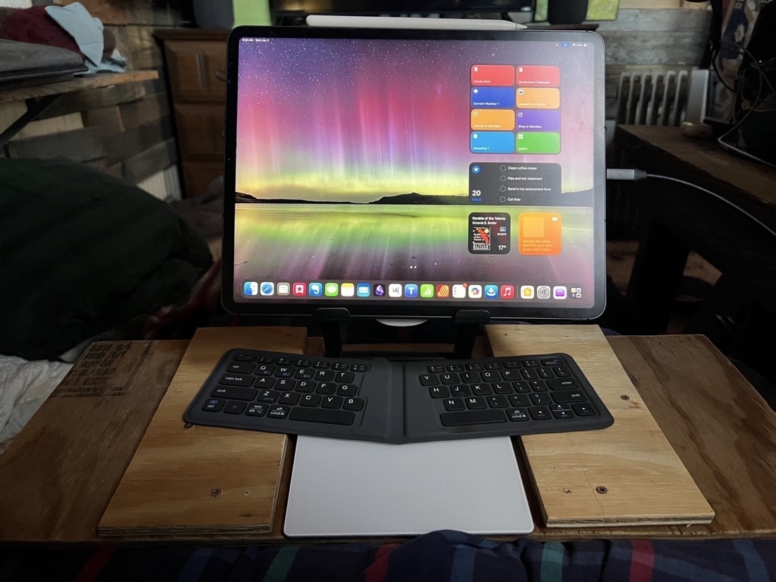 An iPad attached To a stand which is attached to a wooden lap desk. A keyboard and trackpad are below the iPad.