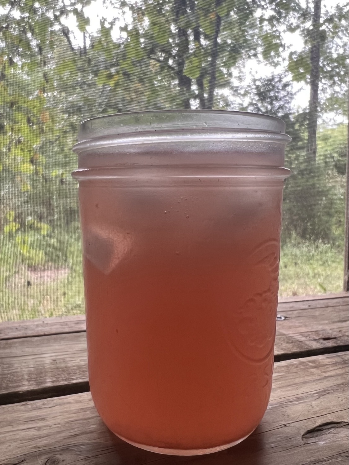 A bright pink drink with ice in a mason jar