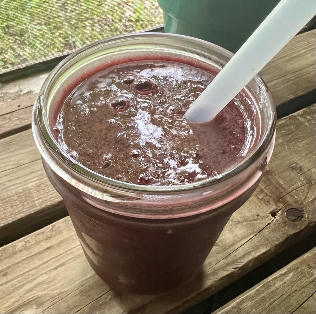 A mason jar of dark purple blackberry smoothie with a straw