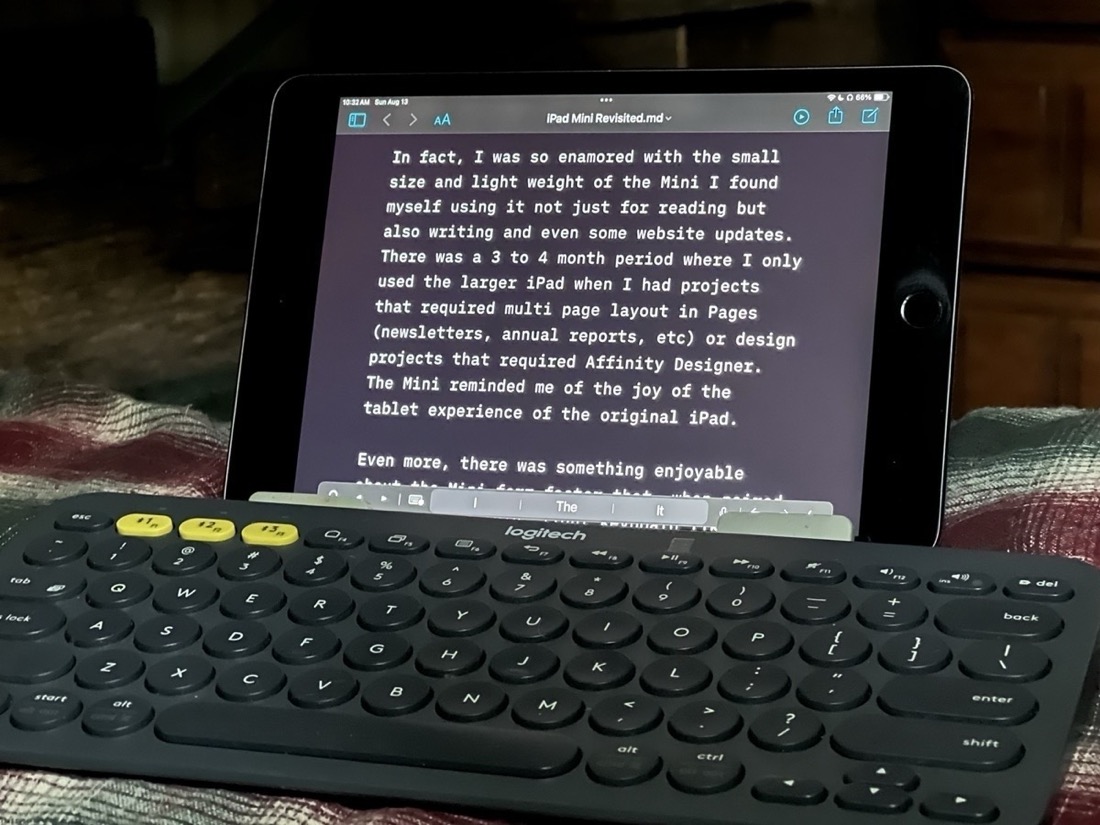 An iPad Mini in a stand sits on a pillow with a black keyboard in front of it