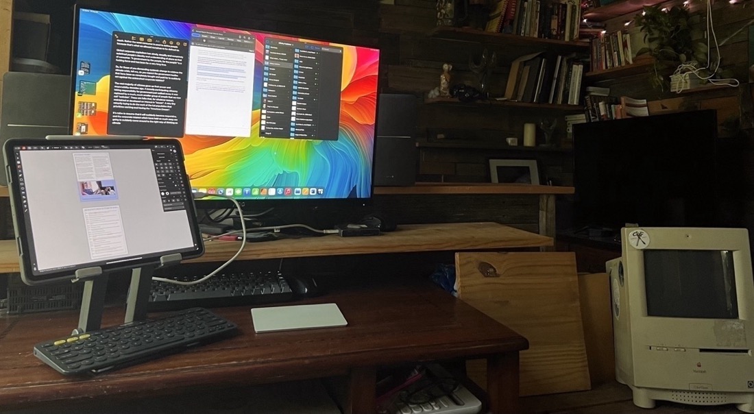 A iPad Pro in a stand sitting next to an external display. There is a keyboard and trackpad in front of the iPad and it is connected to the display